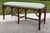 A striking faux bamboo bench featuring a sculptural wood frame with intricate decorative fretwork at the corners and a...