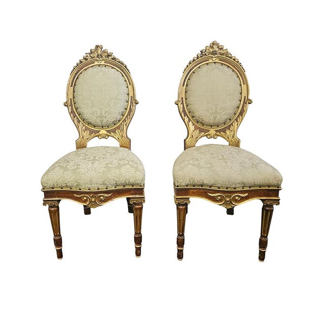 Four lacquered and gilded wooden chairs with a contoured frame carved with plant and scroll motifs, padded and upholstered...