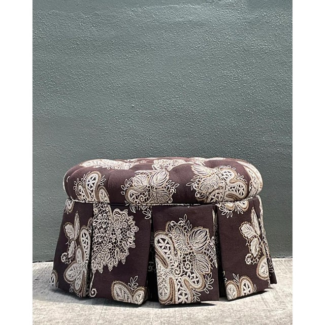 This charming vintage tufted ottoman features a rich fabric displaying a prominent paisley pattern in a subdued color...