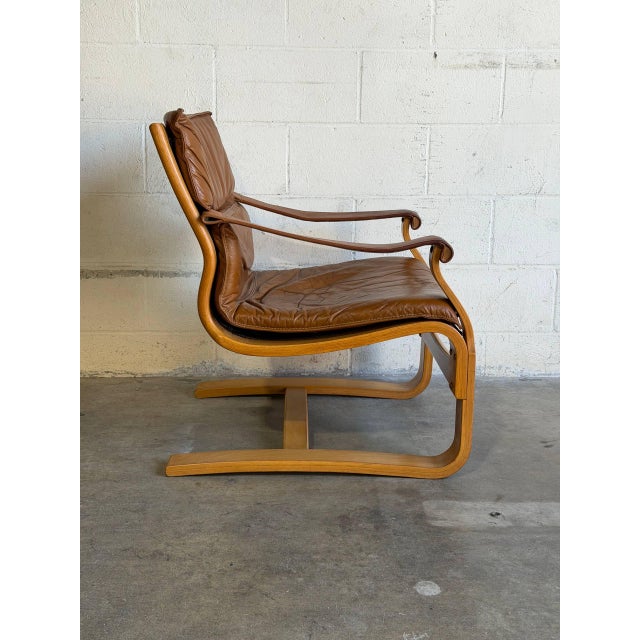 This lounge chair features a cantilevered wood frame with curved armrests and a plush seat cushion. Its organic silhouette...