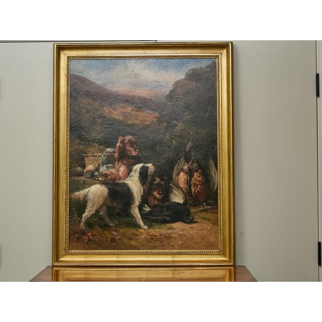 An English oil on canvas hunt painting from the 20th century depicting three dogs and their catch, in carved giltwood...