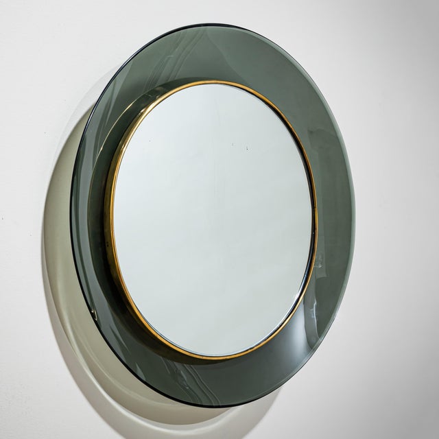 Elegant round wall mirror featuring green-tinted glass with brass accents, designed by Max Ingrand for Fontana Arte. The...