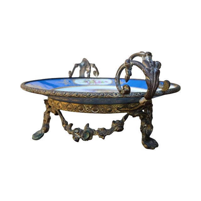 A beautiful antique French porcelain centerpiece displayed in an ornate bronze ormolu stand with elegant scrolling handles...