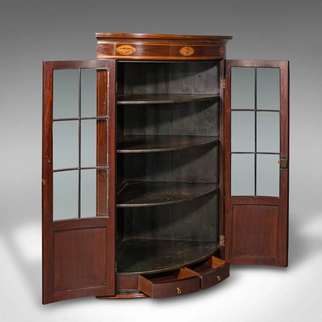 This is an antique glazed corner cabinet. An English, mahogany and glass bow front display cupboard, dating to the...