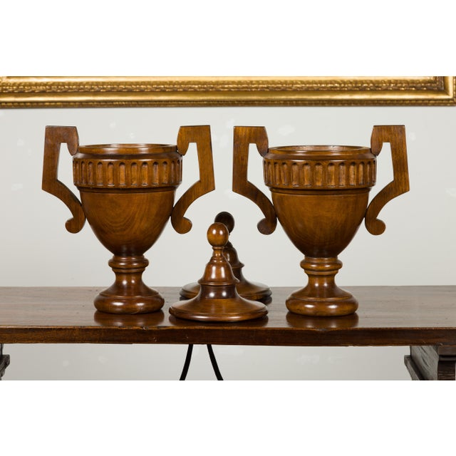 A pair of English vintage carved walnut lidded urns from the mid 20th century, with large handles and fluted motifs....