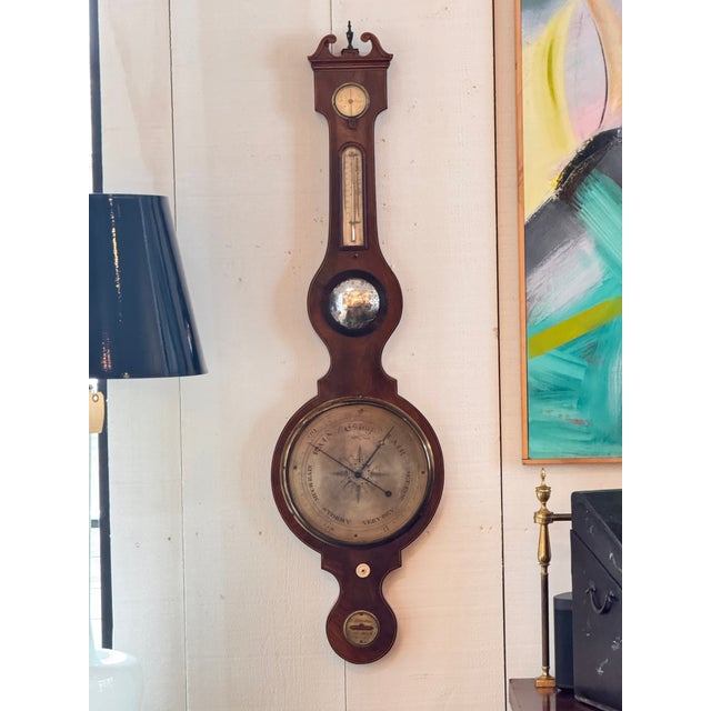 Mahogany wheel barometer with a swan-neck pediment, brass dial, thermometer, hygrometer, and level, with engraved details...
