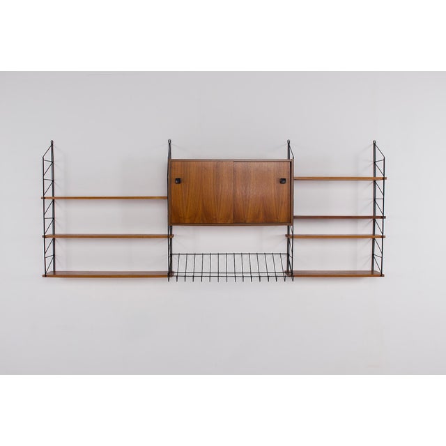 Wall-mounted shelf unit in black steel and teak, dating from the 1950s–1960s. Ladder-style metal frame supporting several...