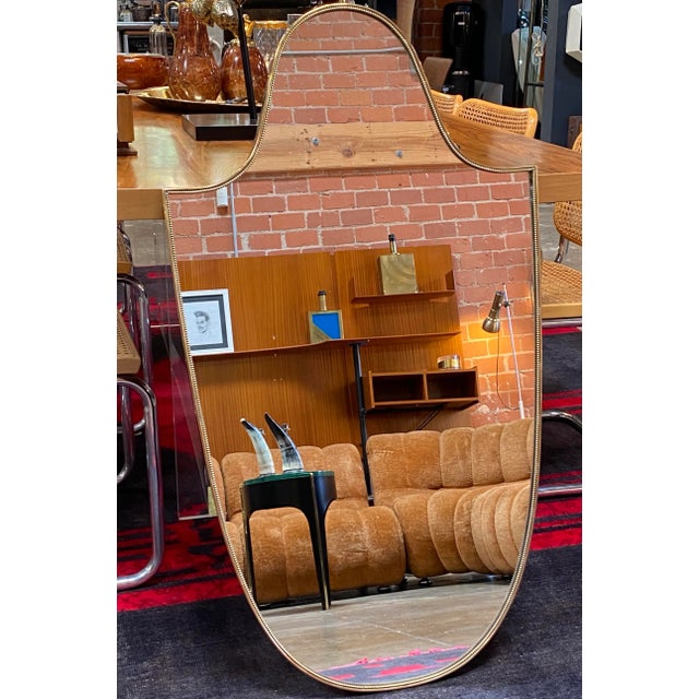 Beautiful Italian Mid-Century wall mirror with an unique shape and brass frame with original patina. AVAILABLE 2