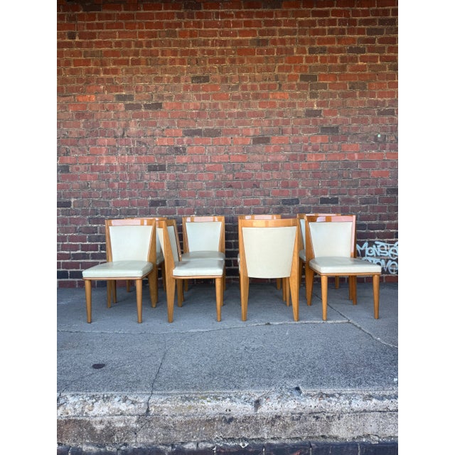 This is a set of 8 Art Deco style dining chairs. They have a tan leather upholstered seat and back with a glossy blonde...