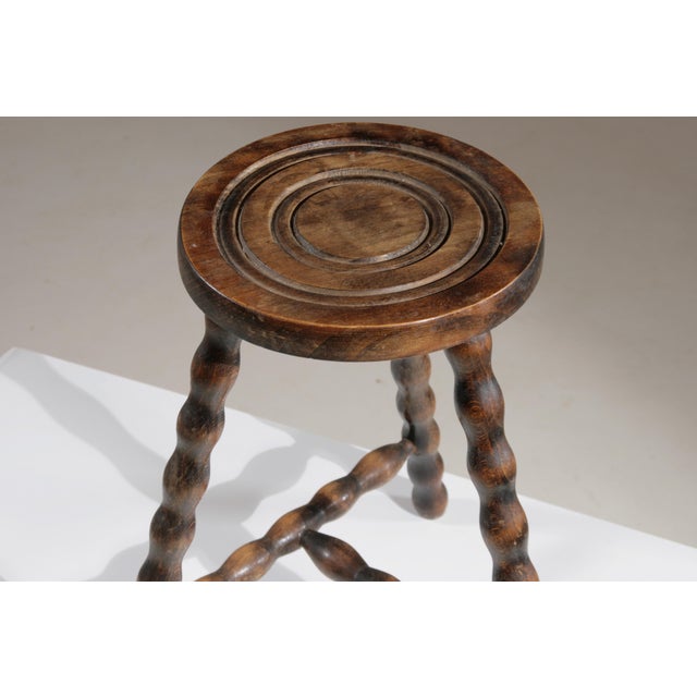 This antique French tripod stool is made of solid wood and is distinguished by its functional design. It features a round...