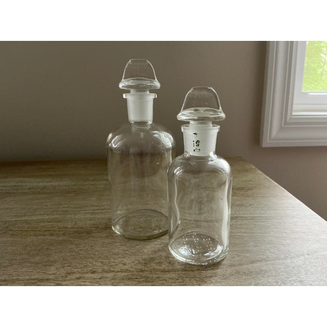 This pair of vintage Pyrex apothecary bottles offers a sleek, industrial-chic aesthetic perfect for a modern vanity, bar...