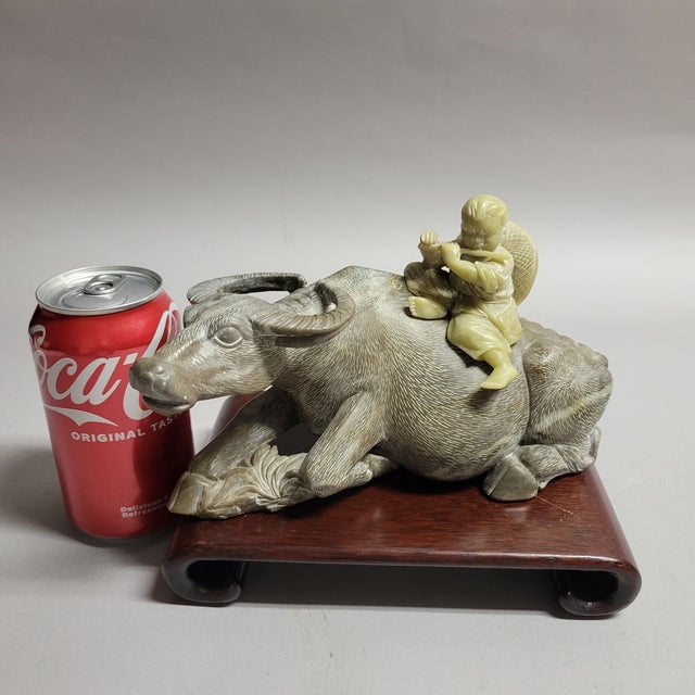 Beautifully detailed stone carving of a Chinese boy playing his bamboo flute while sitting on a resting buffalo. Presented...