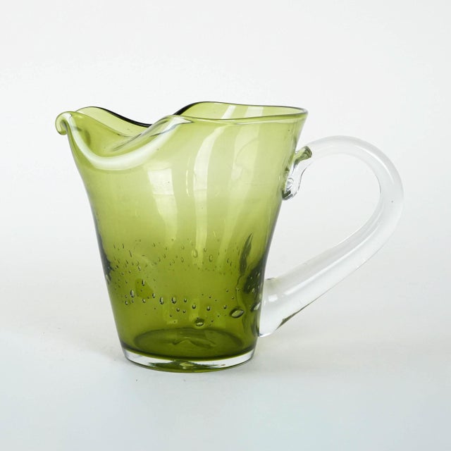 The jug was made in the 1960s in Italy. A glass jug from the 1960s/1970s, handmade from transparent olive-coloured glass....
