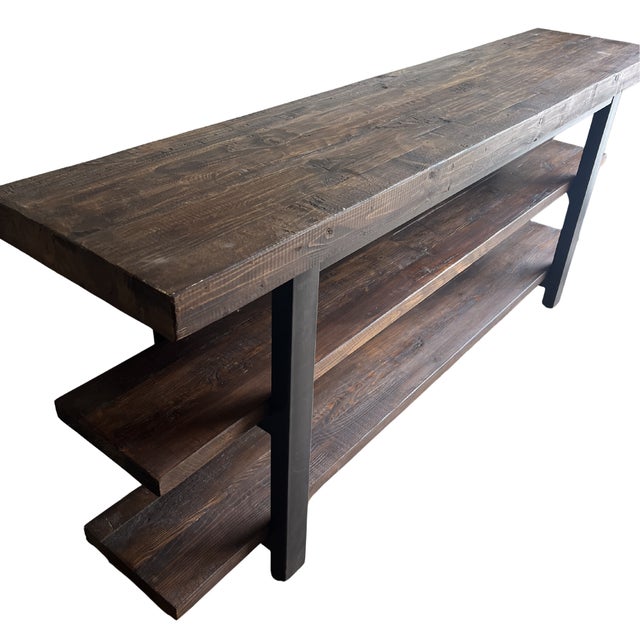 Rustic industrial console or low shelving unit featuring dark stained wood plank shelves and a black metal frame. The...