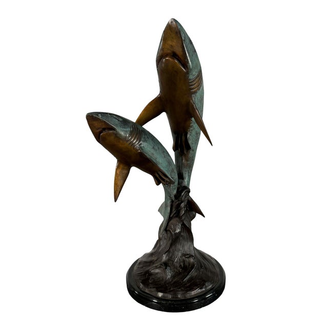Hand cast bronze sculpture featuring two sharks rising dramatically from a wave base. The composition captures the sharks...