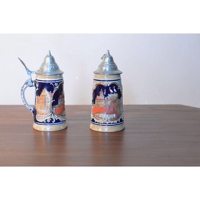 Two German beer steins, or "Bier Steins," decorated with a relief of an Alsatian landscape. Made in Germany circa...