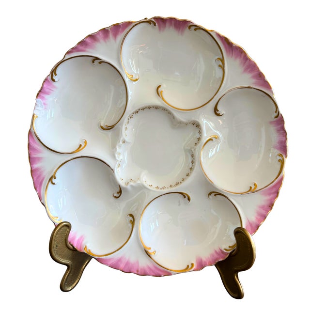A refined Haviland Limoges oyster plate featuring six elegantly shaped wells arranged around a central sauce reserve,...