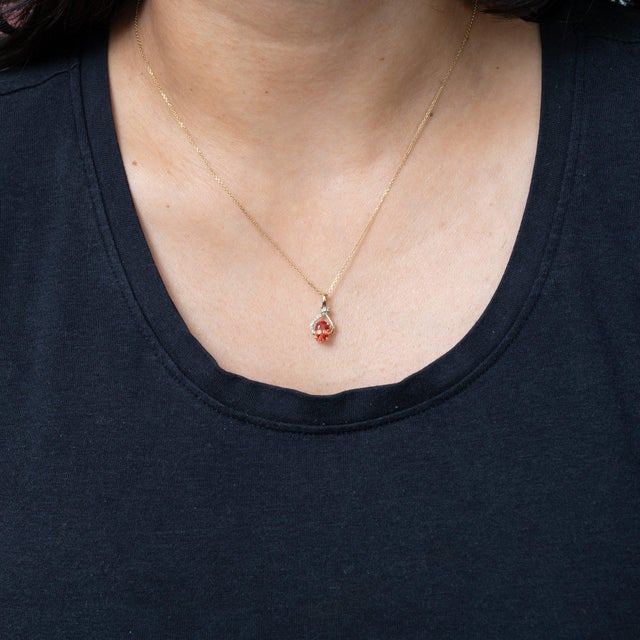 A 1.27-carat padparadscha sapphire oval sits at the centre of this solid 14K yellow gold pendant, framed by thirteen...