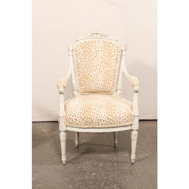 A French pair of Louis XVI style, carved-wood and upholstered armchairs from the 19th century. This antique pair of...
