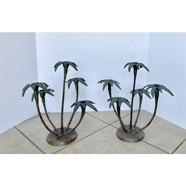 Pair of patinated tole metal palm tree candlestick holders feature sculptural fronds and rocky bases.