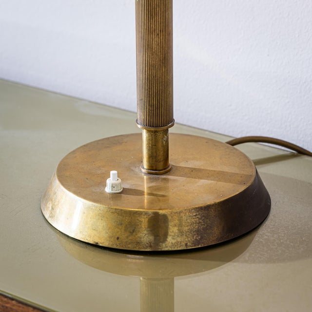 Brass table lamp with an adjustable swivel joint and a smooth conical shade decorated with a diamond-shaped perforated...
