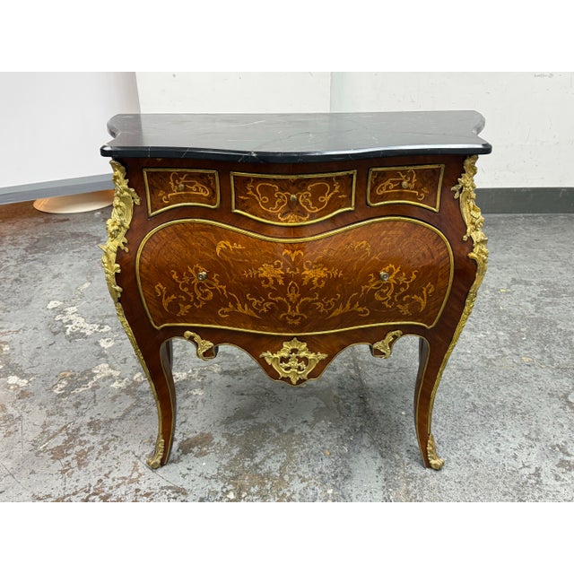 Design Plus Gallery presents a Vintage Louis XV Style Bombe Marquetry Commode. This ornate commode has a bombe case with...