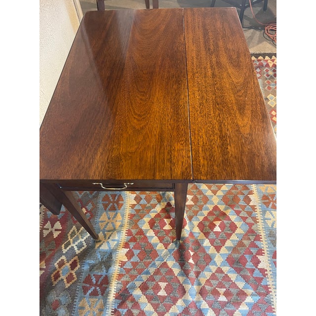 Kindel drop-leaf mahogany side table featuring a drawer, solid brass caster feet, and a functional lock. Each leaf...