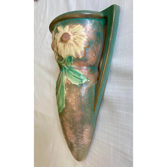 A beautiful arts and crafts Roseville Dahlrose wall pocket with cream colored flowers against a brown textured background....