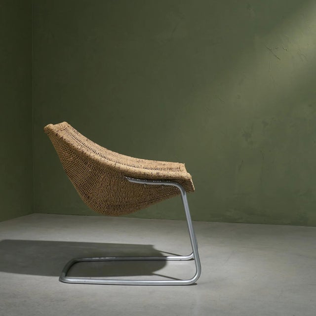 This tubular metal lounge chair features a sisal seating and backrest, creating a unique design where the seat hangs...