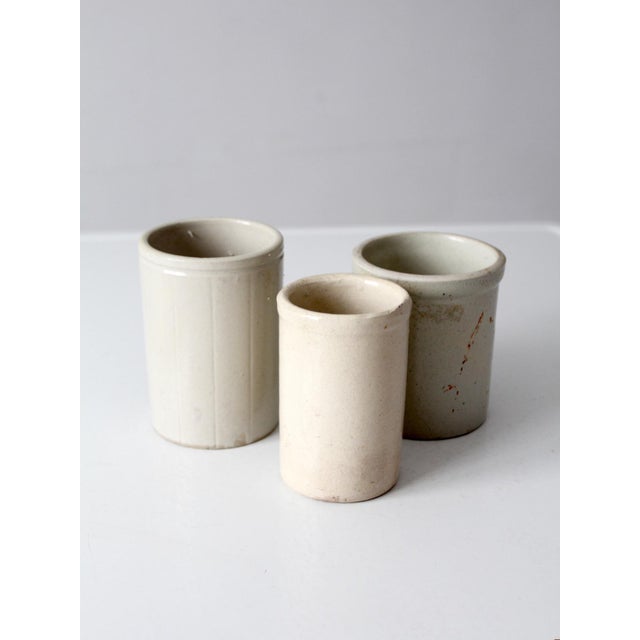 Set of three antique stoneware crocks in softly varied cream and off-white glazes. Each crock has its own subtle...