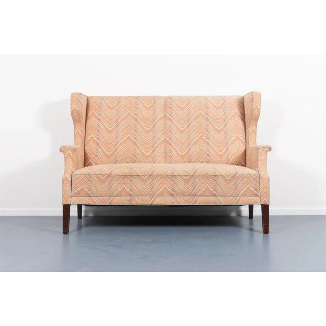 Very beautiful imposing wingback wall sofa on stained wood legs with spectacular colorful fabric upholstery. Produced in...