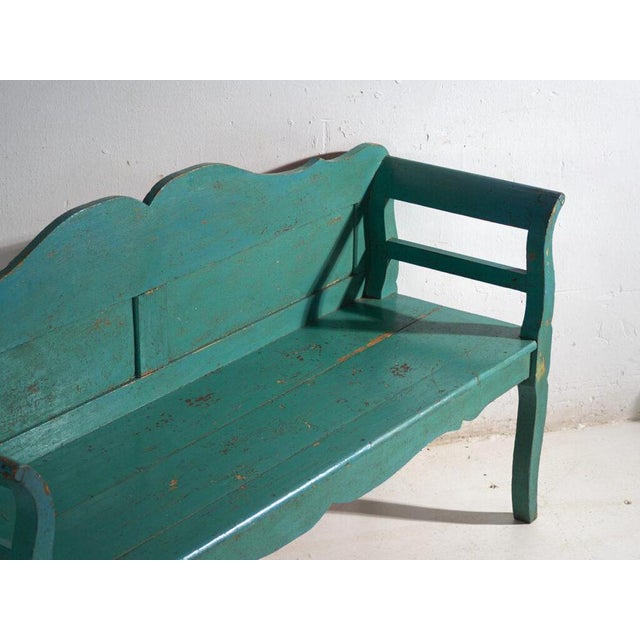 This antique green painted bench in pine wood is a bench with a backrest, a shaped crest rail and armrests, with a...