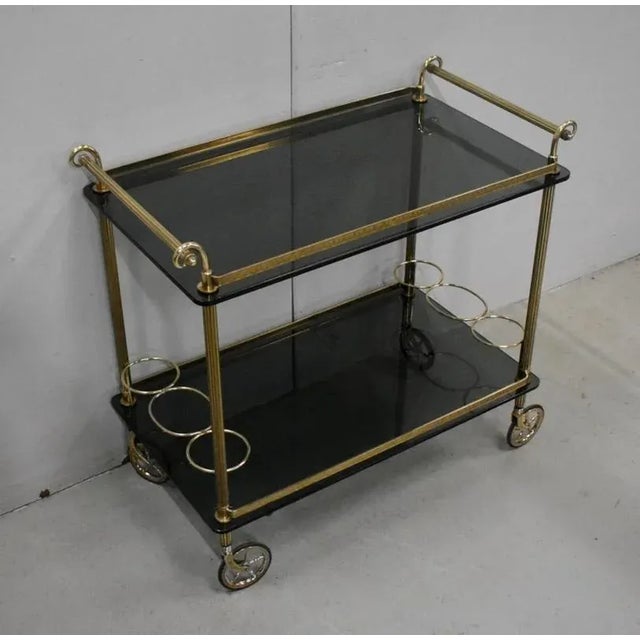 Rolling serving table composed of two similar tops in smoked glass, 7 mm thick, and a brass structure. Two cylindrical...