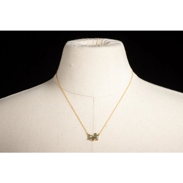 A delicate 14K gold chain necklace featuring a cluster of five emerald-cut green tourmaline gemstones interspersed with...