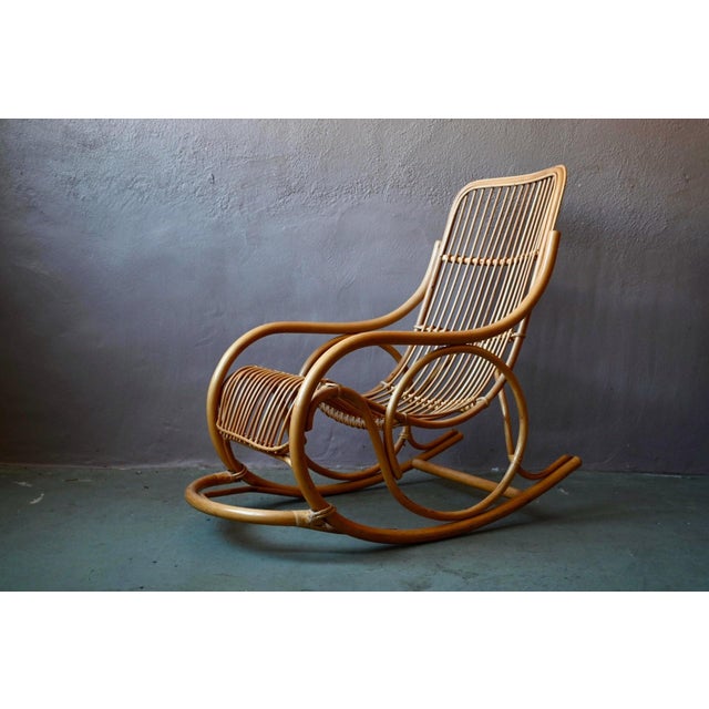 Made entirely of natural rattan, this 1970s rocking chair charms with its light and airy silhouette. The faux leather...