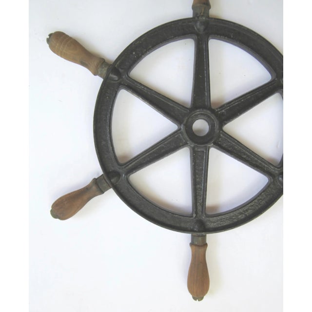Circa 1940s cast iron boat steering wheel in black paint with wood handles, handles have brass screws on ends. No makers...