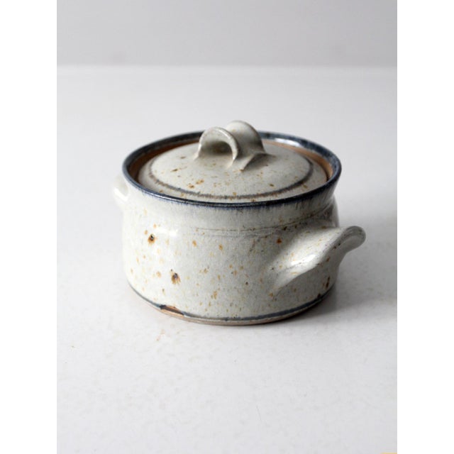 A vintage studio pottery bowl with a softly speckled glaze, blue-gray edging, and organic rust-toned firing marks. The...
