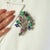 A refined 925 sterling silver floral bouquet brooch pendant featuring natural emeralds, glass-filled blue sapphires, and...