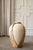 A sculptural vintage terracotta pot encased in an intricately woven rattan frame. The open weave allows the terracotta to...