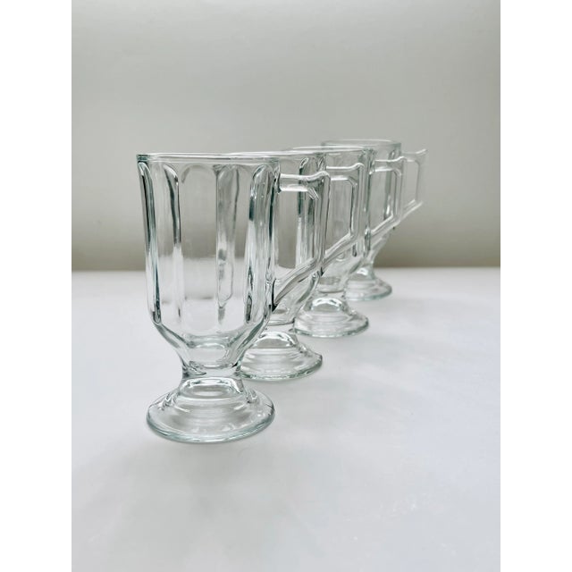 A set of four crisp clear glass footed mugs with a slightly rounded optic pattern with a squared handle made by the Libbey...