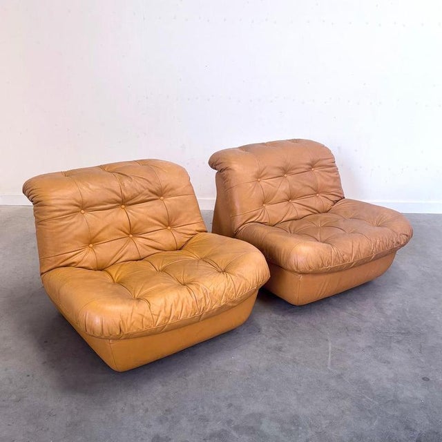 Remarks: Two mid century lounge chairs in space age style, Italy 1970s. Hard foam frames, upholstered in cognac leather....