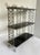 Dating to the mid-20th century, this stylish three-tier display shelf pairs a silver-tone metal frame with glossy black...