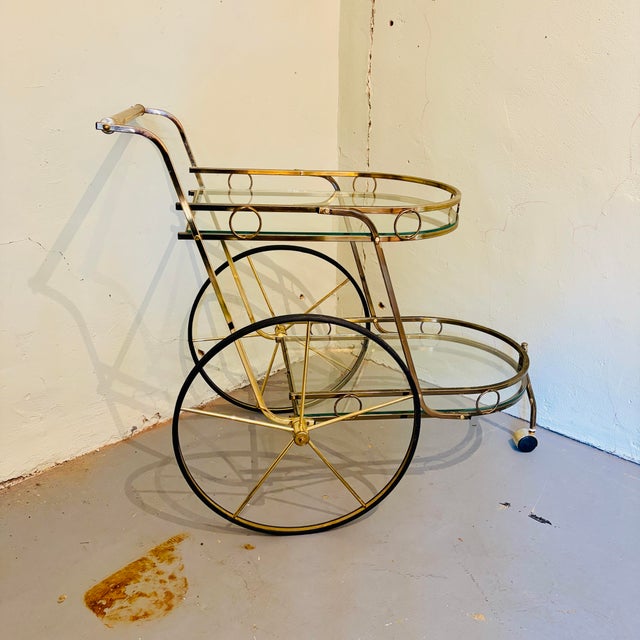 Elegant vintage Hollywood Regency brass and glass bar cart featuring a wonderful two-tier design with rounded fronts,...