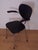 A 1950s chair with a chromed tubular frame, black faux leather seat and back, and black plastic armrests. Its vintage...