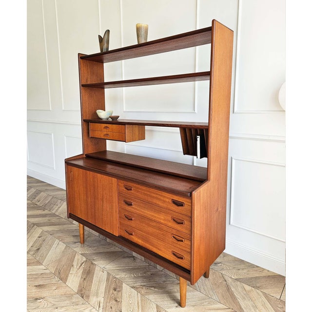 A versatile mid-century bookcase and storage unit with an integrated pull-out writing desk, dating from the 1960s. Crafted...