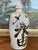A traditional Japanese stoneware sake bottle, featuring hand-brushed calligraphy in dark iron oxide glaze over a warm...