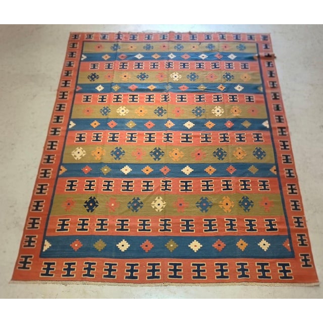 Vintage Persian kilim, circa 1970s, handwoven in a graphic flatweave design. The rug features a warm terracotta-red ground...