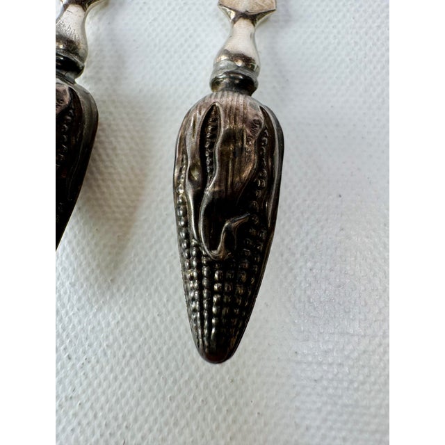 A pair of vintage corn holders with detailed sterling silver handles shaped as ears of corn, complete with individual...