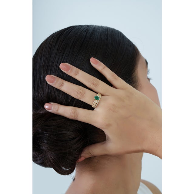 This statement ring features a 0.71 carat oval-cut emerald, set in 18K yellow gold. The emerald measuring approximately 7...