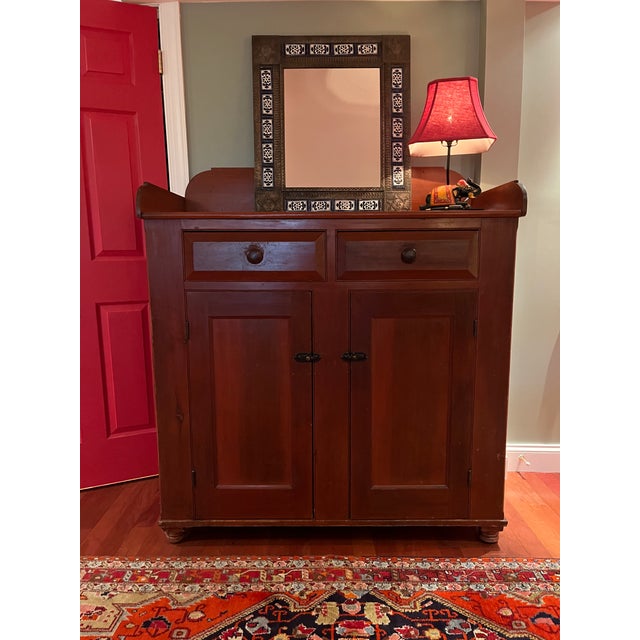 Charming country jelly cupboard is topped by a simple dovetailed gallery that curves at each corner above two beveled...